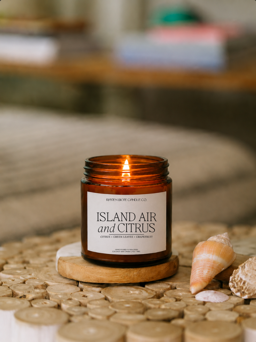 Candle labeled 'Island Air and Citrus' on a woven surface with seashells.