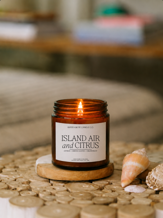 Candle labeled 'Island Air and Citrus' on a woven surface with seashells.