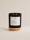 A black double-wick candle in a matte black jar with a white label reading 'VANILLA ORCHID' and a light natural wood base, photographed on a warm off-white background.